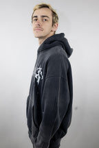 Model wearing a black oversized CyberWaver hoodie with a bold cyber sigil cross design on the back, featuring a distressed stone-wash effect and paint splatter details