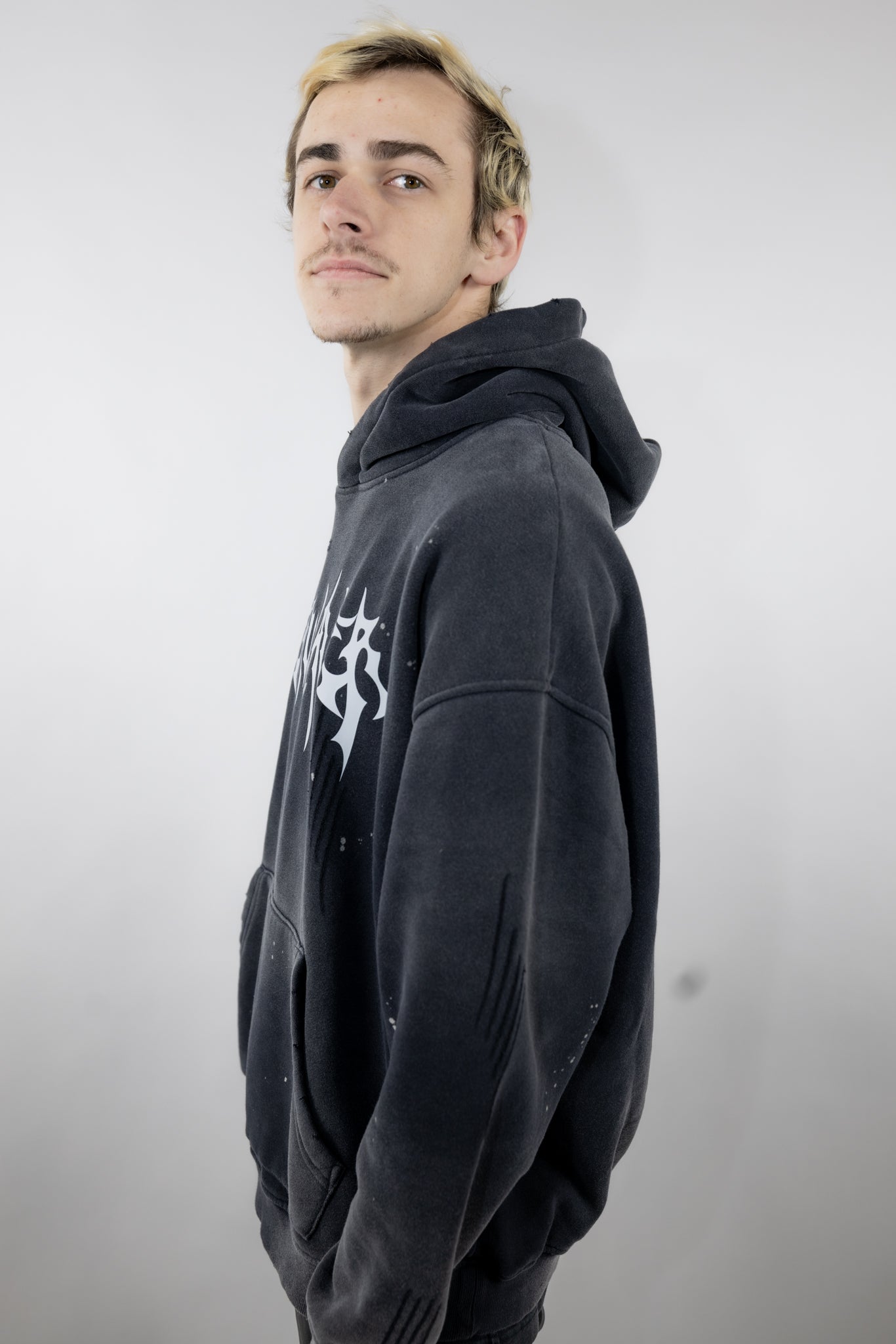 Model wearing a black oversized CyberWaver hoodie with a bold cyber sigil cross design on the back, featuring a distressed stone-wash effect and paint splatter details